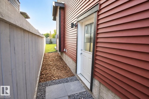 Red horizontal siding with dark trim, white exterior door with window, concrete foundation, and a stone paver pathway - 7274 Morgan Road Nw, Edmonton, AB - Outdoor With Exterior