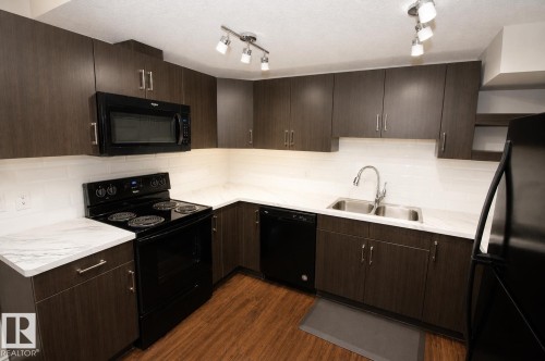 Kitchen featuring dark wood-finish cabinetry, white countertops, white tile backsplash, and wood-finish flooring - 7274 Morgan Road Nw, Edmonton, AB - Indoor Photo Showing Kitchen With Double Sink