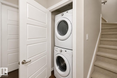 Stackable laundry appliances, carpeted staircase, and panel doors - 7274 Morgan Road Nw, Edmonton, AB - Indoor Photo Showing Laundry Room