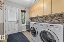 Functional laundry area featuring light wood-finish upper cabinetry, a patterned tile backsplash, and a dark countertop - 