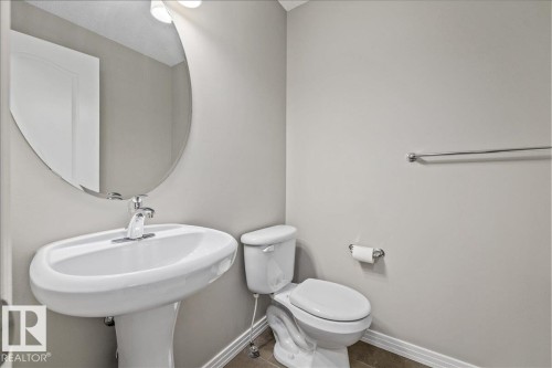 Pedestal sink with chrome faucet, oval mirror, and white toilet - 1086 Grantham Drive Nw, Edmonton, AB - Indoor Photo Showing Bathroom