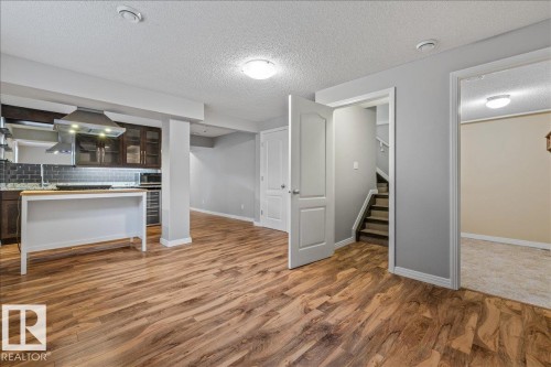 Open-concept kitchen area featuring wood-finish flooring, dark cabinetry, subway tile backsplash, and a white island with a butcher block top - 1086 Grantham Drive Nw, Edmonton, AB - Indoor Photo Showing Other Room