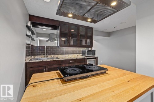 Kitchenette featuring a wood-finish countertop with a built-in cooktop, dark wood-finish cabinetry with glass-front uppers, granite-style countertops, and a subway tile backsplash - 1086 Grantham Drive Nw, Edmonton, AB - Indoor Photo Showing Kitchen
