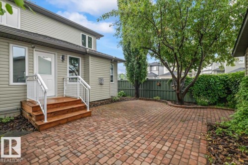 Expansive paver patio featuring a raised wood deck with white railings, mature trees, and privacy fencing - 1086 Grantham Drive Nw, Edmonton, AB - Outdoor