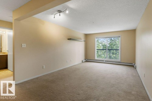 Sliding glass door, track lighting fixture, wall-mounted shelving, neutral-toned carpeting, and a balcony with an iron railing - #307 1188 Hyndman Rd Nw, Edmonton, AB - Indoor Photo Showing Other Room