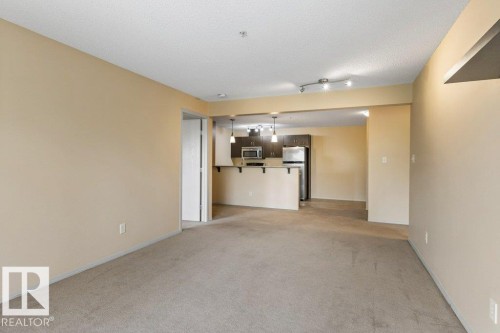 Open-concept living area featuring a kitchen with dark wood-finish cabinetry, stainless steel appliances, and a breakfast bar - #307 1188 Hyndman Rd Nw, Edmonton, AB - Indoor Photo Showing Other Room