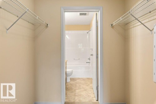 White wire shelving systems, light beige wall paint, tile flooring, white bathtub and shower surround, and a white toilet - #307 1188 Hyndman Rd Nw, Edmonton, AB - Indoor Photo Showing Other Room