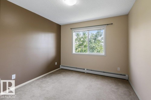 Carpeted room featuring a large window, neutral wall tones, and overhead lighting - #307 1188 Hyndman Rd Nw, Edmonton, AB - Indoor Photo Showing Other Room