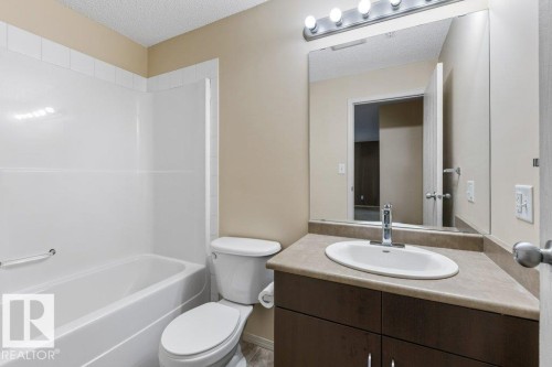Bathroom featuring an integrated bathtub and shower, dark wood-finish vanity with a laminate countertop, and a large mirror with overhead lighting - #307 1188 Hyndman Rd Nw, Edmonton, AB - Indoor Photo Showing Bathroom