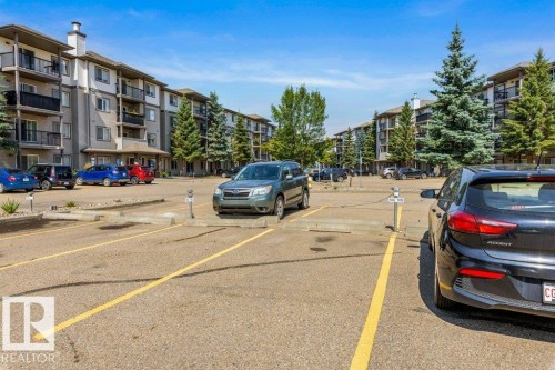 Multi-story residential buildings with balconies, paved parking area, and mature evergreen trees - #307 1188 Hyndman Rd Nw, Edmonton, AB - Outdoor