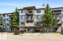Multi-level building with individual balconies, prominent evergreen landscaping, ample exterior parking, and a stone-clad entrance - #307 1188 Hyndman Rd Nw, Edmonton, AB  - Outdoor With Balcony With Facade 