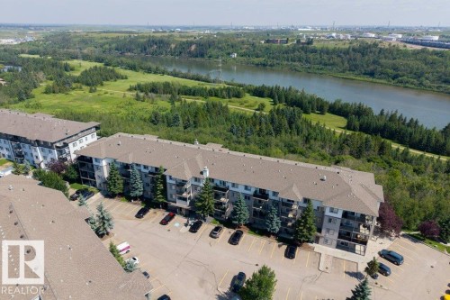 Multi-story residential buildings with balconies, surface parking, and surrounding mature trees, set against a river and extensive green space - #307 1188 Hyndman Rd Nw, Edmonton, AB - Outdoor With Body Of Water With View