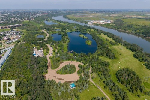 Meandering river, multiple lakes, extensive green spaces, mature tree cover, and residential areas in the background - #307 1188 Hyndman Rd Nw, Edmonton, AB - Outdoor With Body Of Water With View