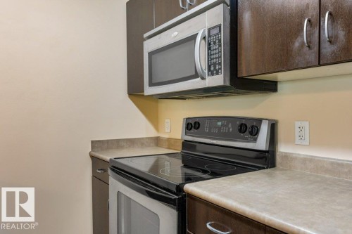 Stainless steel oven with a flat cooktop, microwave, and dark wood-finish cabinetry - #307 1188 Hyndman Rd Nw, Edmonton, AB - Indoor Photo Showing Kitchen