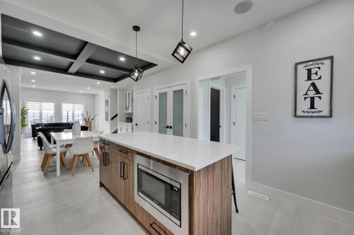 Central kitchen island with a light-toned countertop, wood-finish cabinetry, and an integrated microwave - 51 Clichy Close, St. Albert, AB - Indoor Photo Showing Kitchen