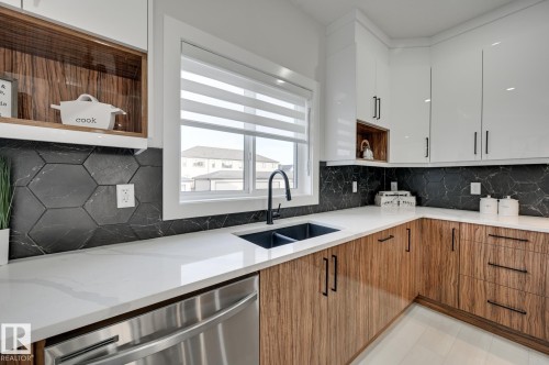 White upper cabinetry, wood-finish lower cabinetry, hexagonal dark tile backsplash, white countertops, and a black double basin sink - 51 Clichy Close, St. Albert, AB - Indoor Photo Showing Kitchen With Double Sink With Upgraded Kitchen
