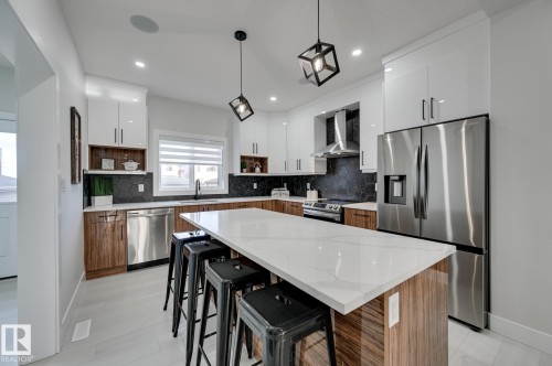 Kitchen featuring a large central island with a light-toned countertop, two-toned cabinetry, stainless steel appliances, black hexagonal tile backsplash, and recessed lighting - 51 Clichy Close, St. Albert, AB - Indoor Photo Showing Kitchen With Stainless Steel Kitchen With Upgraded Kitchen