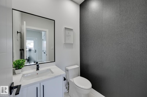 White vanity with integrated sink, black-framed mirror, contemporary black faucet, and textured accent wall - 51 Clichy Close, St. Albert, AB - Indoor Photo Showing Bathroom
