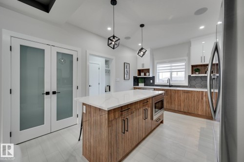 Kitchen featuring a central island with quartz countertops, wood-finish cabinetry, stainless steel appliances, and hexagon tile backsplash - 51 Clichy Close, St. Albert, AB - Indoor Photo Showing Kitchen