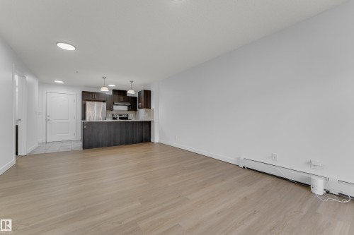 Wood-finish flooring throughout, complemented by a kitchen featuring dark wood cabinetry, a breakfast bar, and stainless steel appliances - #217 667 Watt Bv Sw, Edmonton, AB - Indoor