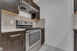 Dark wood-finish cabinetry, stainless steel range with overhead ventilation, light-toned countertop, horizontal tile backsplash, and tile flooring - 