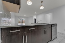 Kitchen island featuring dark wood-finish cabinetry, light-toned countertops, an undermount sink with a gooseneck faucet, a built-in stainless steel dishwasher, and two pendant light fixtures - 