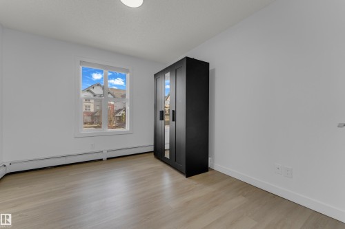 Light wood-finish flooring, white walls, and a large window providing natural light - #217 667 Watt Bv Sw, Edmonton, AB - Indoor Photo Showing Other Room