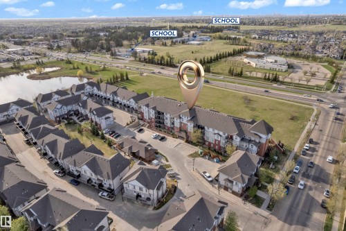 Townhome community with varied architectural styles, a pond, and adjacent green spaces - #217 667 Watt Bv Sw, Edmonton, AB - Outdoor With View