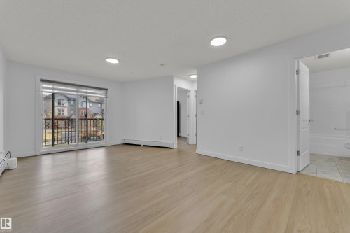 Light wood-finish flooring, white walls, recessed ceiling lighting, and a private balcony with black metal railings - #217 667 Watt Bv Sw, Edmonton, AB - Indoor Photo Showing Living Room