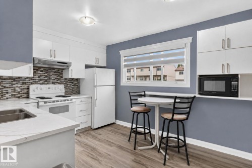Kitchen featuring white cabinetry, wood-finish flooring, a mosaic tile backsplash, white countertops, and a double basin sink - 1344 Lakewood Road West Nw, Edmonton, AB - Indoor Photo Showing Kitchen With Double Sink