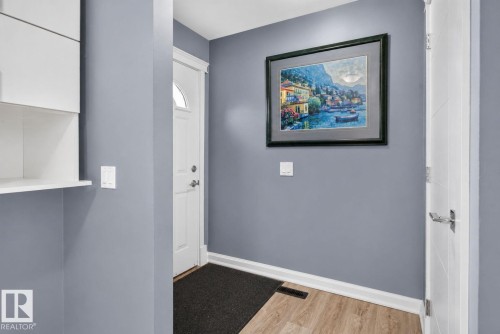 Entryway featuring wood-finish flooring, crisp white baseboards, and a modern white door with an arched window insert - 1344 Lakewood Road West Nw, Edmonton, AB - Indoor Photo Showing Other Room