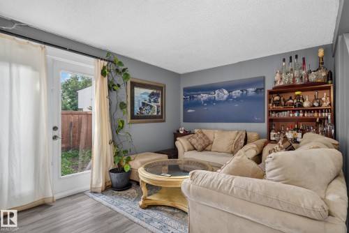 Living area featuring wood-finish flooring, a glass-paned door, and a built-in wooden shelving unit - 1344 Lakewood Road West Nw, Edmonton, AB - Indoor Photo Showing Living Room