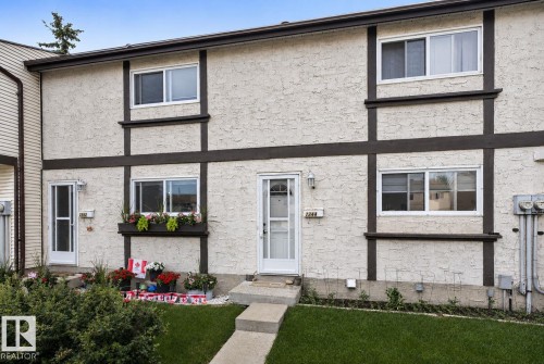 Stucco exterior with decorative dark trim, white frame windows, an individual entry door, a concrete pathway, and a grassy front yard - 1344 Lakewood Road West Nw, Edmonton, AB - Outdoor