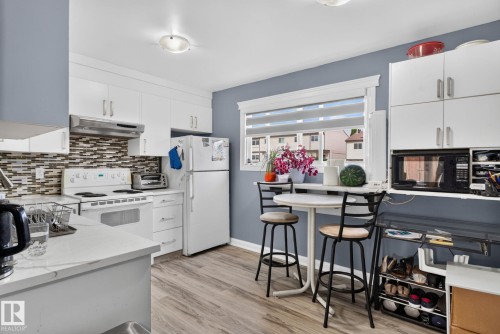 Kitchen featuring white cabinetry, light-toned wood-finish flooring, a tile backsplash, and a window with blinds - 1344 Lakewood Road West Nw, Edmonton, AB - Indoor Photo Showing Kitchen