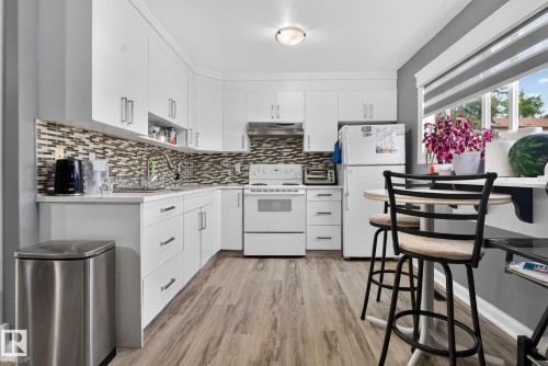 Kitchen featuring white cabinetry with silver-tone hardware, a mosaic tile backsplash, wood-finish flooring, and a large window - 1344 Lakewood Road West Nw, Edmonton, AB - Indoor Photo Showing Kitchen With Upgraded Kitchen
