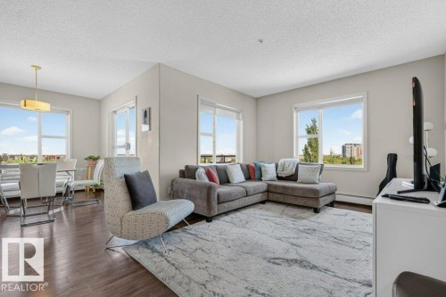 Hardwood-finish flooring, multiple large windows, recessed ceiling lighting, and a modern gold-toned pendant light fixture - #423 320 Ambleside Li Sw, Edmonton, AB - Indoor Photo Showing Living Room