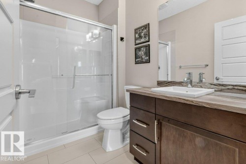 Walk-in shower with clear glass enclosure, a white rectangular vessel sink, dark wood-finish vanity with drawer storage, and a large wall-mounted mirror - #423 320 Ambleside Li Sw, Edmonton, AB - Indoor Photo Showing Bathroom