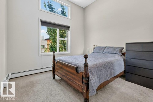 Vaulted ceiling, upper transom window, large window with roller shade, wall-to-wall carpeting, and baseboard heating - #423 320 Ambleside Li Sw, Edmonton, AB - Indoor Photo Showing Bedroom