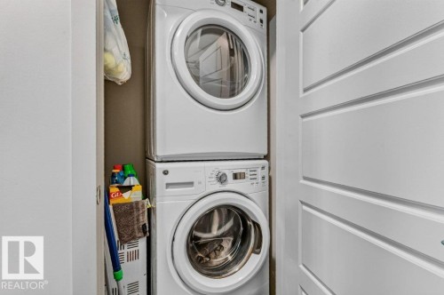 Stacked laundry center featuring two full-size front-load washers and dryers in white, providing convenient in-home clothing care - #423 320 Ambleside Li Sw, Edmonton, AB - Indoor Photo Showing Laundry Room