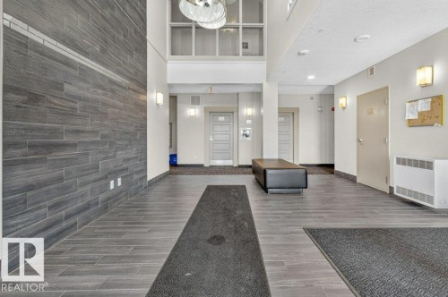Lobby entry featuring plank-style tile flooring, a multi-story ceiling, and sconce lighting - #423 320 Ambleside Li Sw, Edmonton, AB - Indoor Photo Showing Other Room
