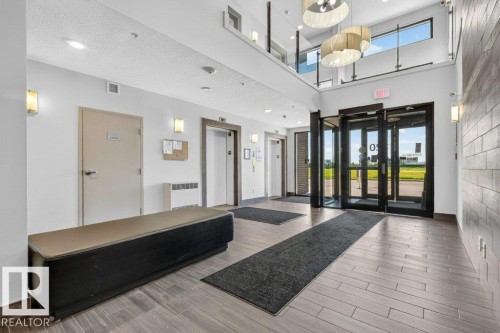 Modern lobby featuring soaring ceilings with clerestory windows, polished wood-finish flooring, and sleek black aluminum-frame glass entry doors - #423 320 Ambleside Li Sw, Edmonton, AB - Indoor Photo Showing Other Room