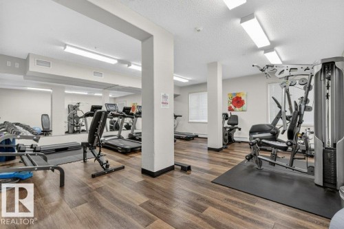 Fitness center with wood-finish flooring, mirrored wall, and recessed lighting - #423 320 Ambleside Li Sw, Edmonton, AB - Indoor Photo Showing Gym Room