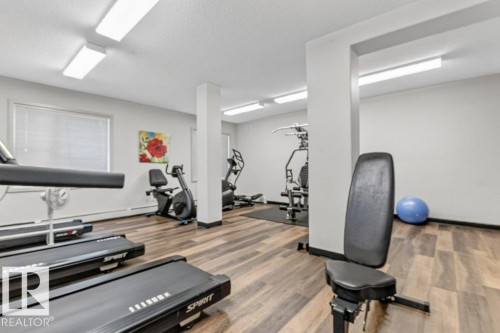 State-of-the-art fitness facility featuring multiple cardio and strength training stations, wood-finish flooring throughout, recessed ceiling lighting, and bright, open layout with structural support columns - #423 320 Ambleside Li Sw, Edmonton, AB - Indoor Photo Showing Gym Room