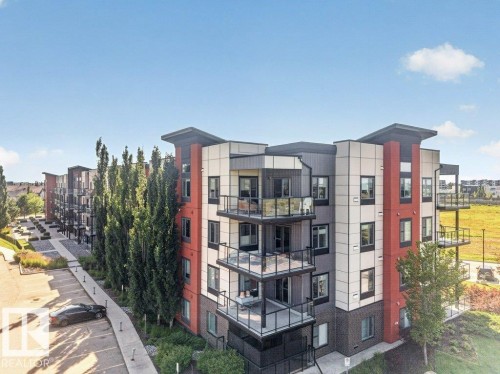 Multi-story building featuring contemporary exterior finishes, private balconies with glass railings, landscaped grounds, and paved parking - #423 320 Ambleside Li Sw, Edmonton, AB - Outdoor With Balcony