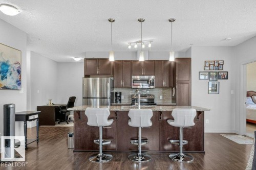 Kitchen with dark wood-finish cabinetry, stainless steel appliances, and a central island with a stone countertop - #423 320 Ambleside Li Sw, Edmonton, AB - Indoor Photo Showing Kitchen With Upgraded Kitchen