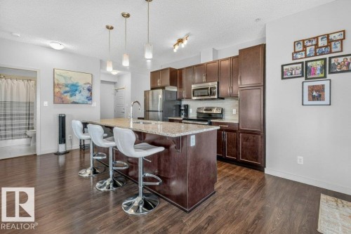 Contemporary kitchen and dining area featuring custom wood cabinetry, stainless steel appliances, quartz countertops, and a center island with seating - #423 320 Ambleside Li Sw, Edmonton, AB - Indoor Photo Showing Kitchen With Upgraded Kitchen