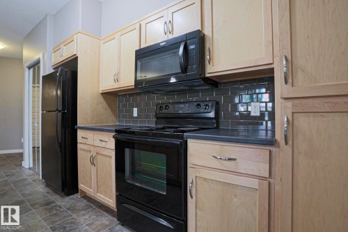 Kitchen featuring light wood cabinetry, black appliances, dark subway tile backsplash, and dark countertops - #209 304 Ambleside Link Li Sw Sw, Edmonton, AB - Indoor Photo Showing Kitchen