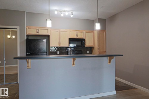 Kitchen featuring light-toned cabinetry, dark-toned backsplash, black appliances, and a gray countertop - #209 304 Ambleside Link Li Sw Sw, Edmonton, AB - Indoor Photo Showing Kitchen