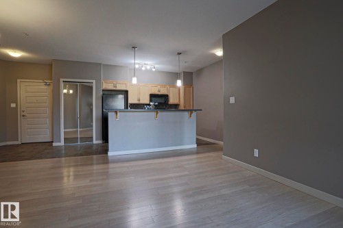 Kitchen featuring light wood-finish cabinetry, black appliances, a tiled backsplash, and a breakfast bar with pendant lighting - #209 304 Ambleside Link Li Sw Sw, Edmonton, AB - Indoor Photo Showing Kitchen