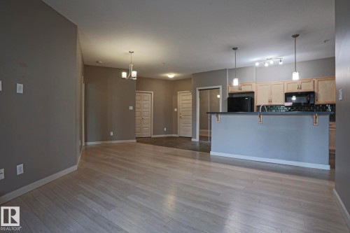 Open-concept living area showcasing wood-finish flooring throughout, pendant lighting, and a kitchen island with blue cabinetry - #209 304 Ambleside Link Li Sw Sw, Edmonton, AB - Indoor Photo Showing Kitchen